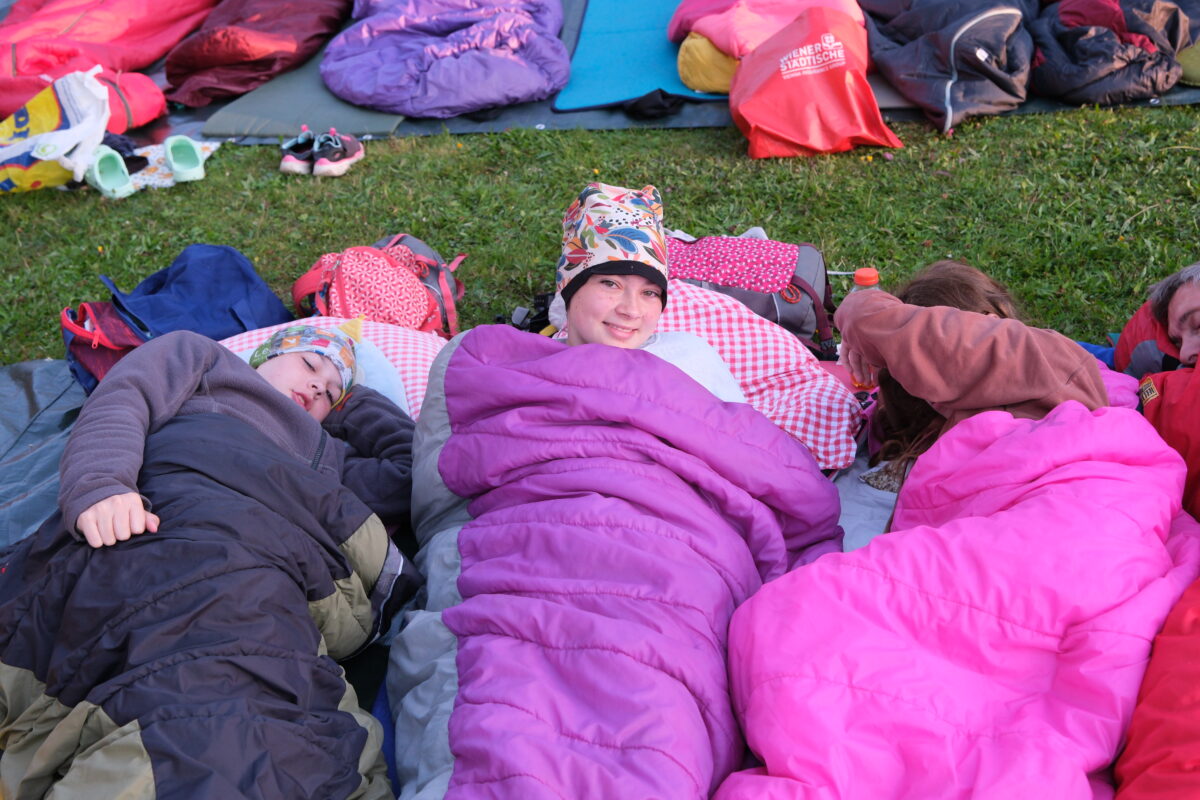 Schlafende Menschen auf einer Wiese im Freien, eingekuschelt in ihre Schlafsäcke.