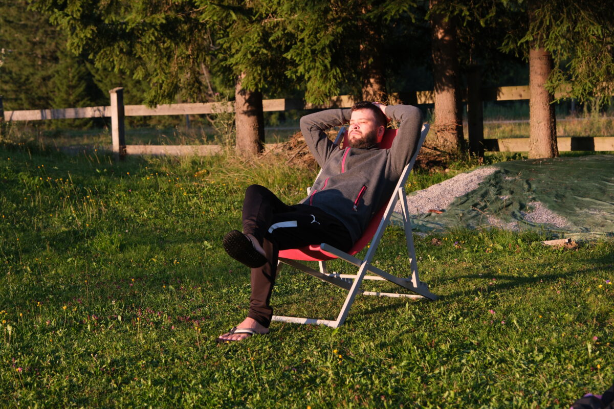 In der Natur sitzt ein Mann im Liegestuhl und genießt die Abendsonne.