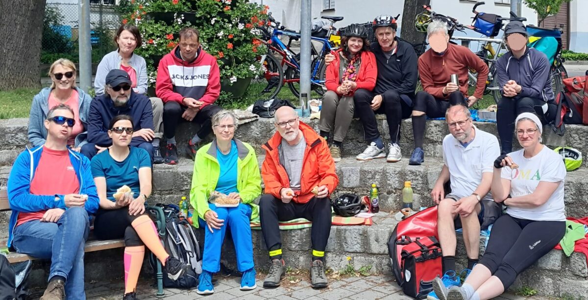 Eine Gruppe von Menschen in Freizeitbekleidung und Fahrrädern, die eine Pause machen und auf Steinstufen sitzen.