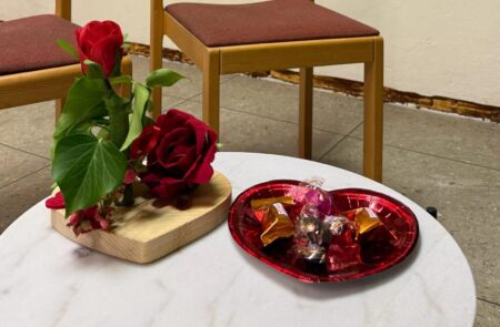 liebevoll dekoriertet Tisch für den Paarabend mit Rose und Herzschale mit Süßigkeiten darauf.