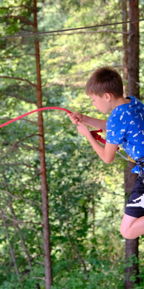 Junge springt gerade ab beim Seilsprung in eine Schlucht. Er ist mit einem Gurt am Seil gesichert.