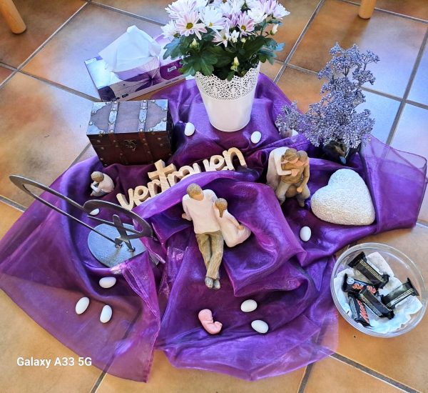 Auf einem violetten Seidentuch liegen arrangiert verschiedene Symbole für Vertrauen.