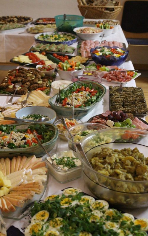 reichhaltiges Buffet mit verschiedenen Platten angerichtet. Gemischte Salate, Kartoffelsalat, gekochte Eierplatte, Käse, Wurstvarianten, Tomaten, Aufstriche, schön dekoriert.